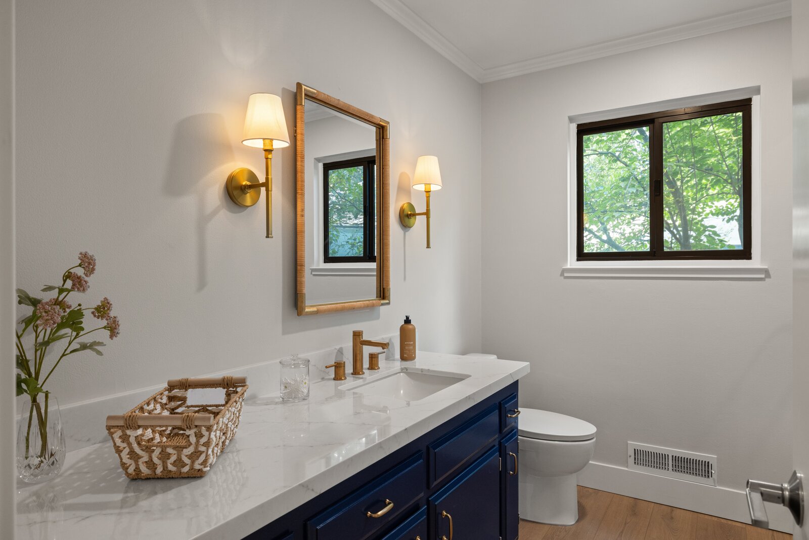 Bathroom remodel in Sacramento, CA with navy vanity, brass fixtures, and woven mirror