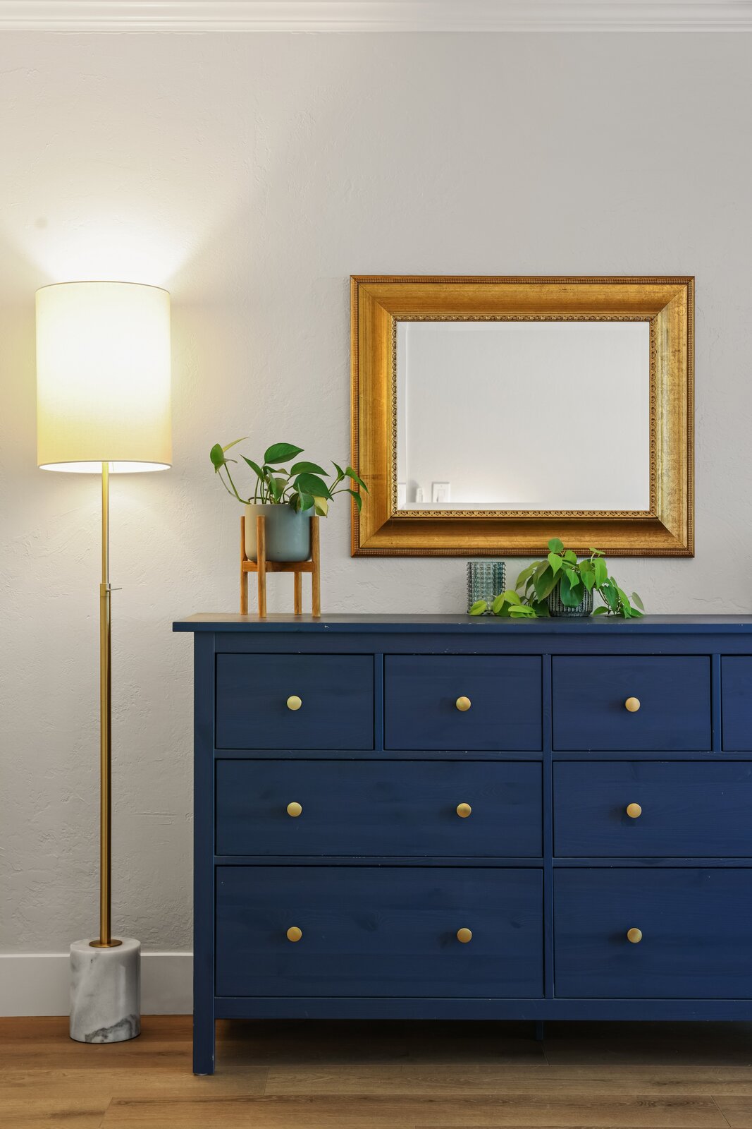 Sacramento area bedroom with navy blue dresser, gold mirror, and brass floor lamp