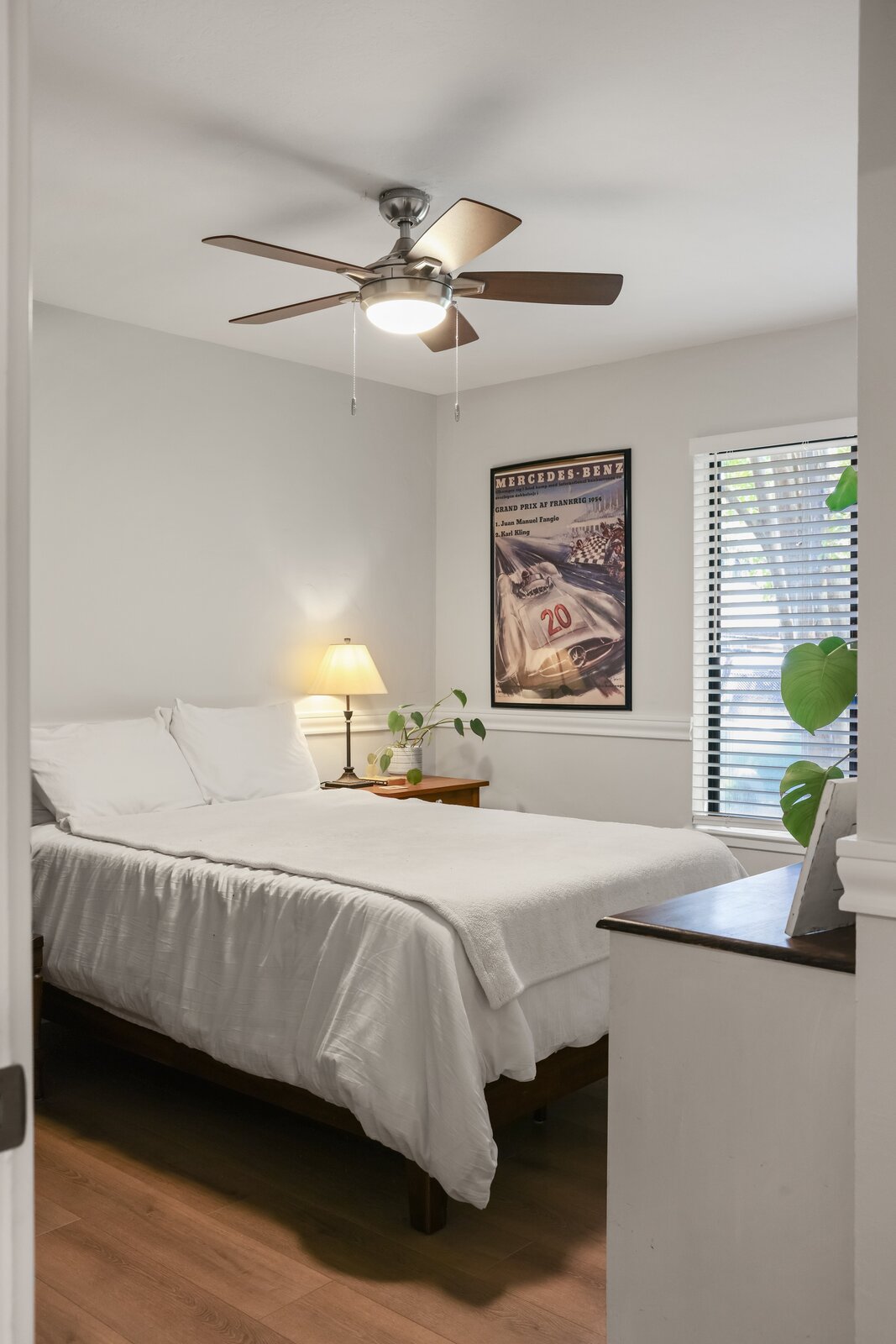 Sacramento area bedroom with white bedding, wood nightstand, and vintage racing poster