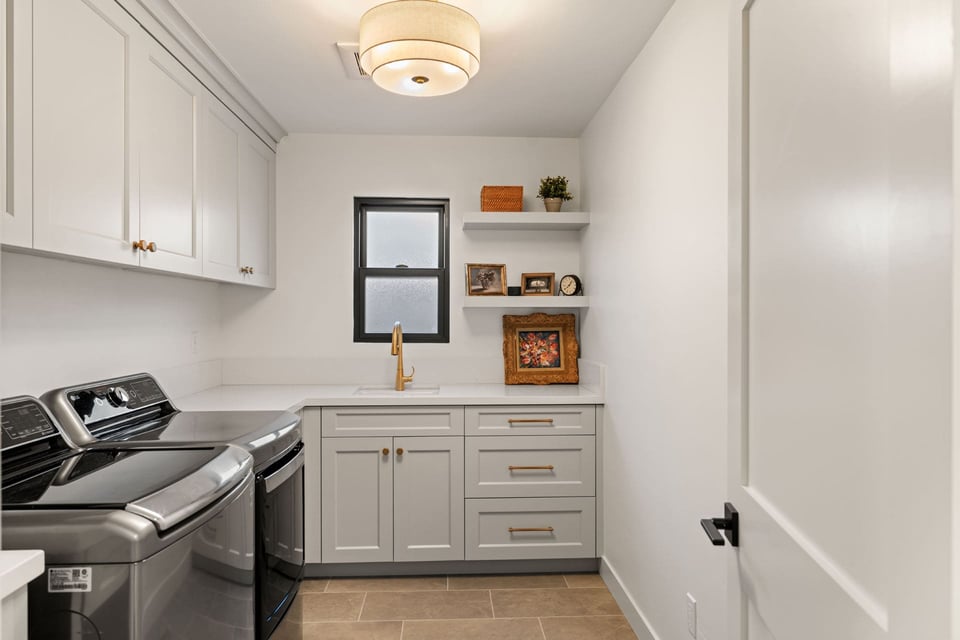 Laundry room by H&H Builds in Sacramento with stainless steel appliances, gray cabinetry, and gold faucet under window
