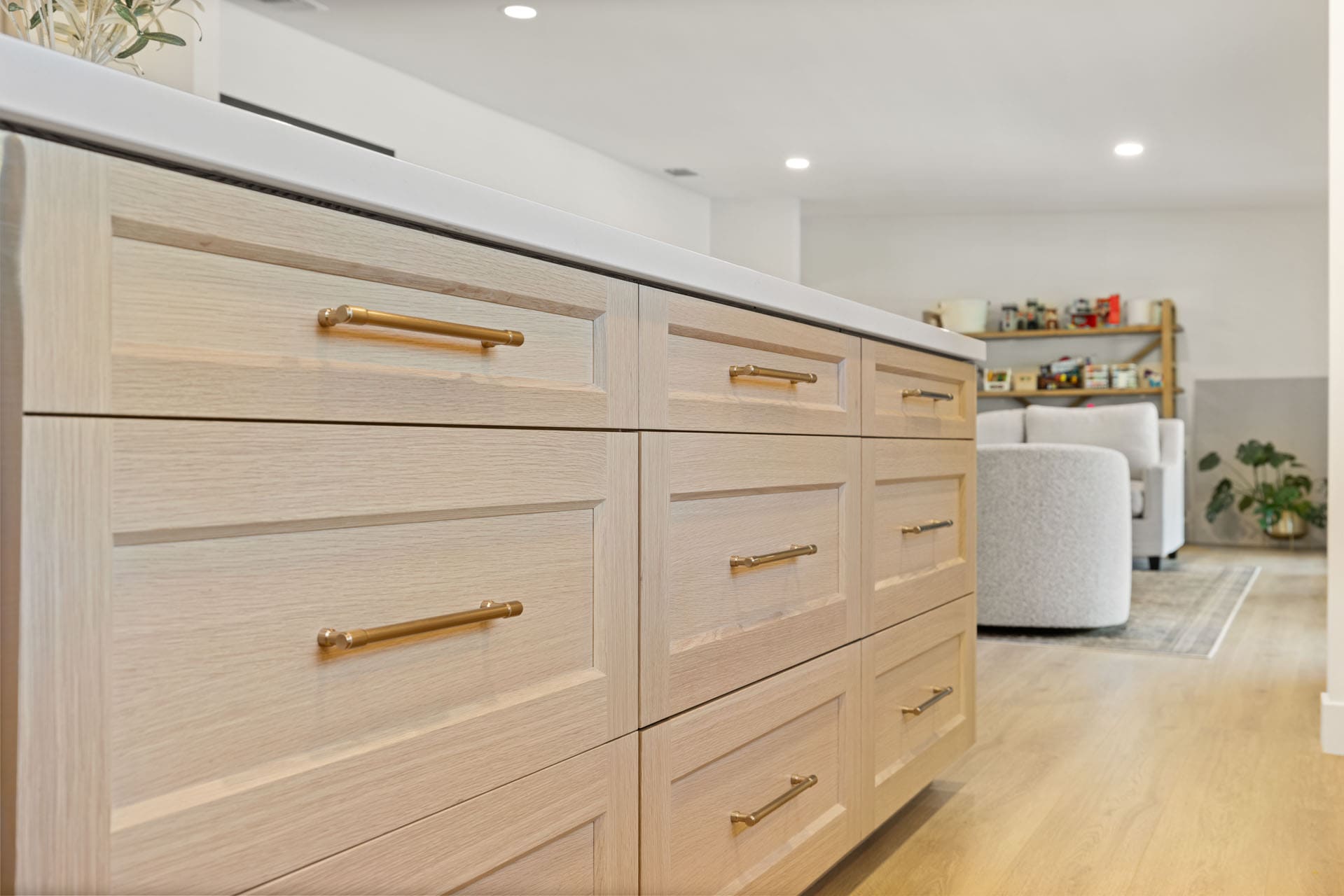 Light wood kitchen island by H&H Builds in Sacramento with brass handles and drawers facing an open living room.