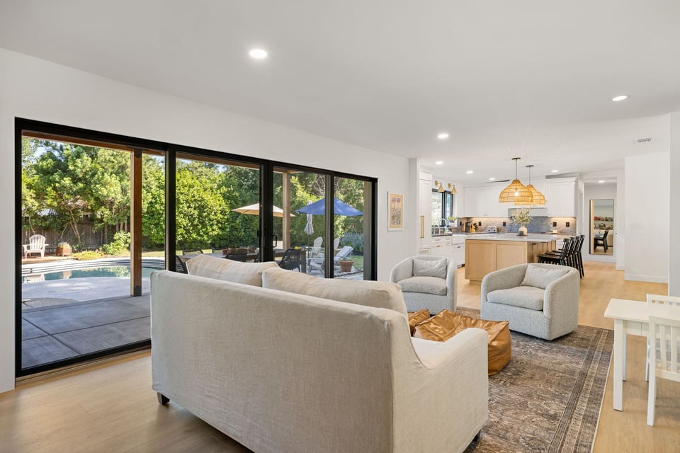 Living area by H&H Builds in Sacramento with wide sliders to pool, lounge seating, and open flow to a white and wood kitchen