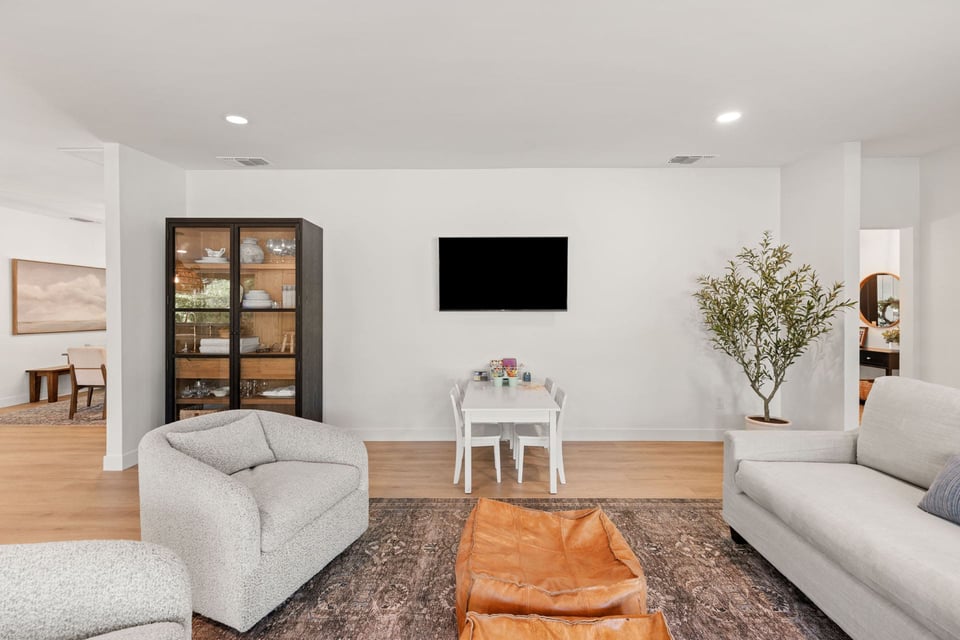 Living room in Sacramento featuring modern chairs, a display cabinet, and table below wall-mounted TV by H&H Builds