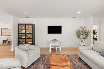 Living room in Sacramento featuring How Long Does it Take to Build a Custom Home in Sacramento?modern chairs, a display cabinet, and table below wall-mounted TV by H&H Builds