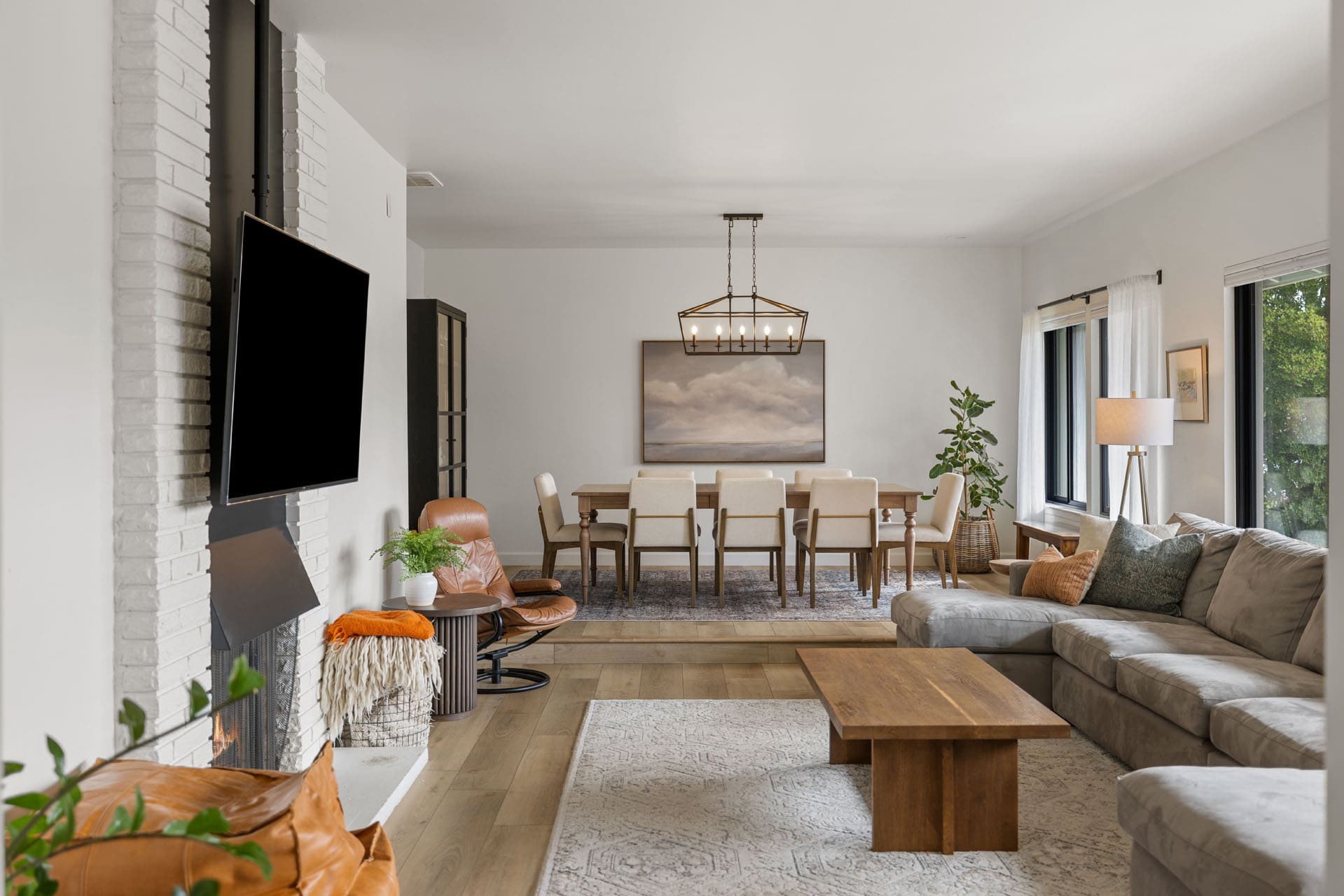 BEFORE dining and lounge space with wood table, chandelier, fireplace, and neutral sectional sofa