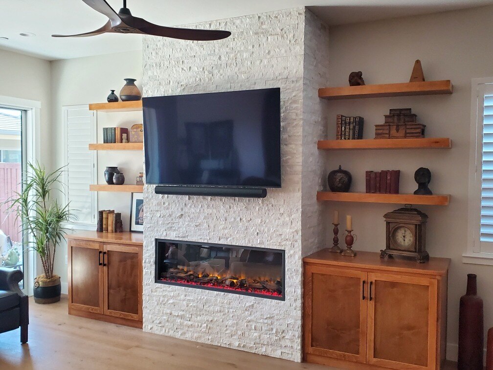 Renovated living room with natural wood cabinets, decorative shelving, and a stone fireplace by H&H Builds, Sacramento, CA