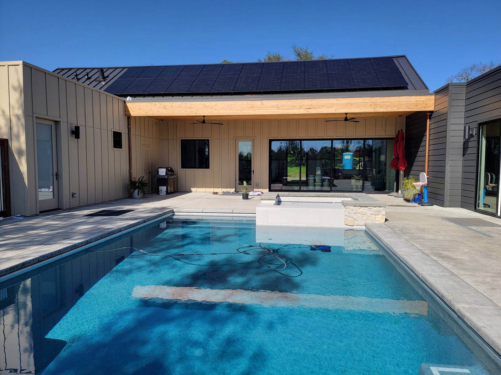 Backyard remodel with a sparkling pool, spa, and modern covered patio with solar panels by H&H Builds in Sacramento, CA