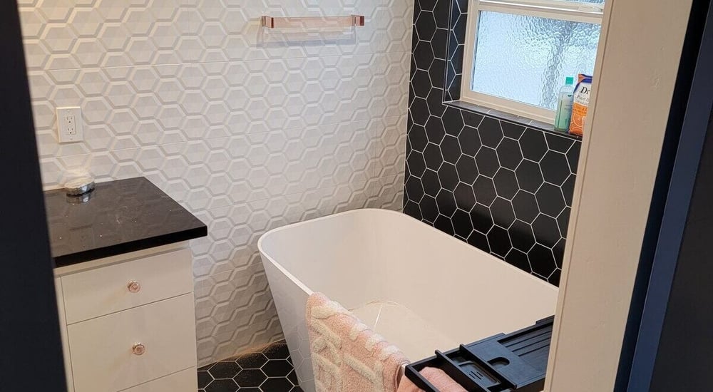 Modern bathroom remodel with a white freestanding tub, black hexagon tile floors, and geometric wall tiles by H&H Builds in Sacramento, CA