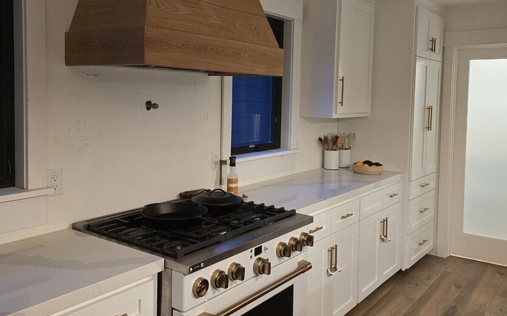 Modern kitchen remodel featuring white cabinetry, gold hardware, and a custom wooden range hood in Sacramento, CA, by H&H Builds