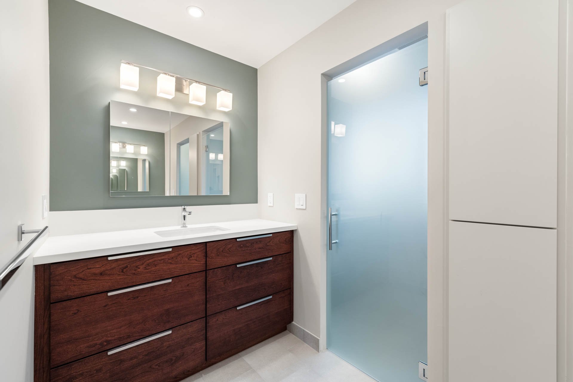 Remodeled Sacramento bathroom vanity with green accent wall, mirror, and frosted glass door