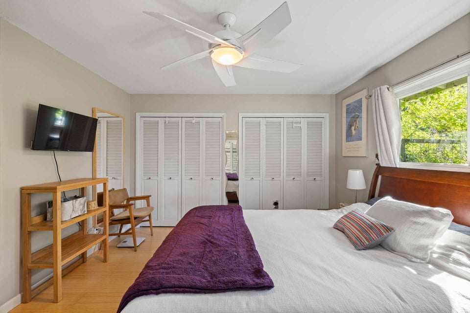 Sacramento bedroom with TV, wooden shelf, and louvered closet doors near a window with leafy view