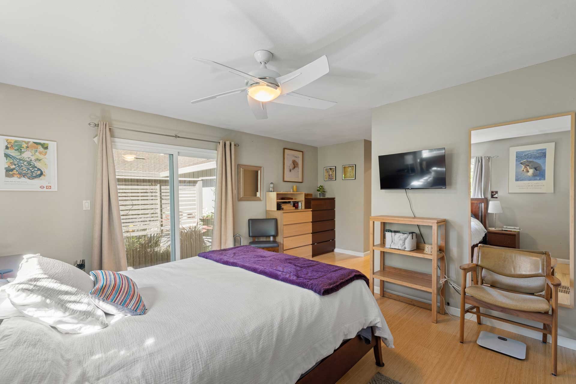Sacramento bedroom with sliding glass door, flat-screen TV, dresser, and bed with a purple blanket and striped pillow