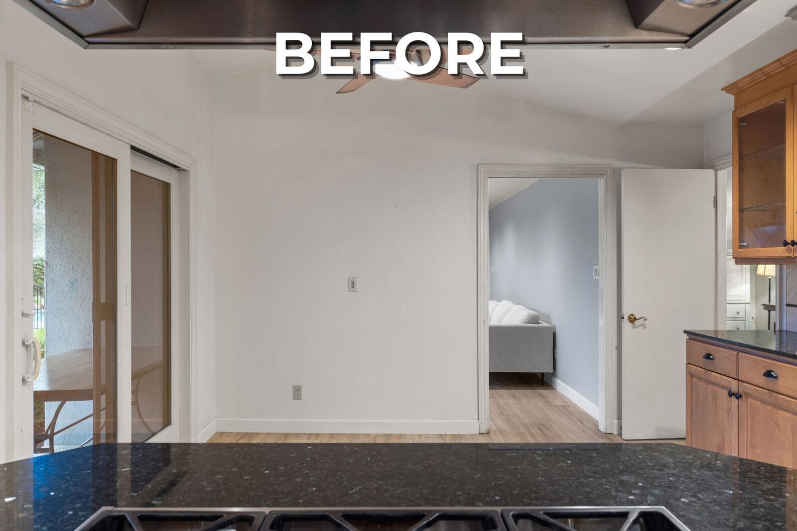 Before - Closed kitchen view with dark stone counters, wood cabinetry, sliding glass door, and a narrow opening to the living room. Before - Closed kitchen view with dark stone counters, wood cabinetry, sliding glass door, and a narrow opening to the living room.