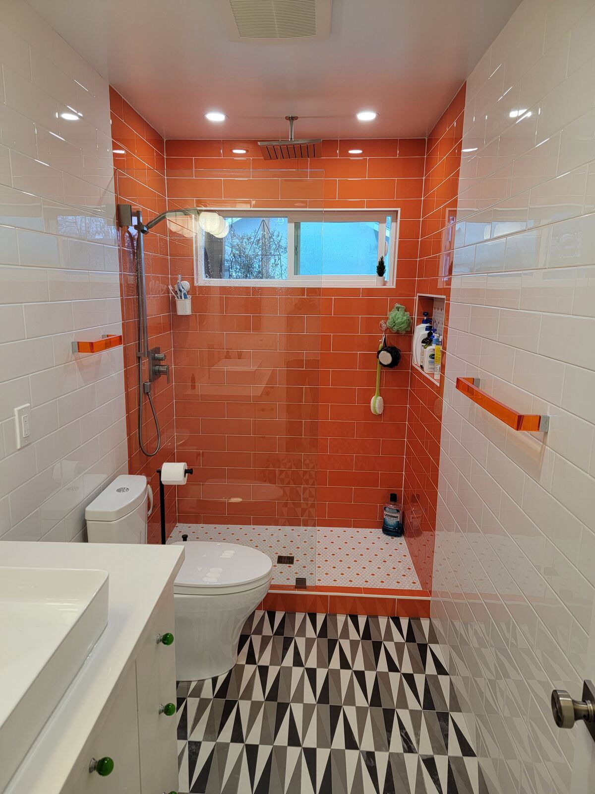 Bold modern bathroom remodel with bright orange shower tiles and black-and-white patterned flooring by H&H Builds, Sacramento, CA