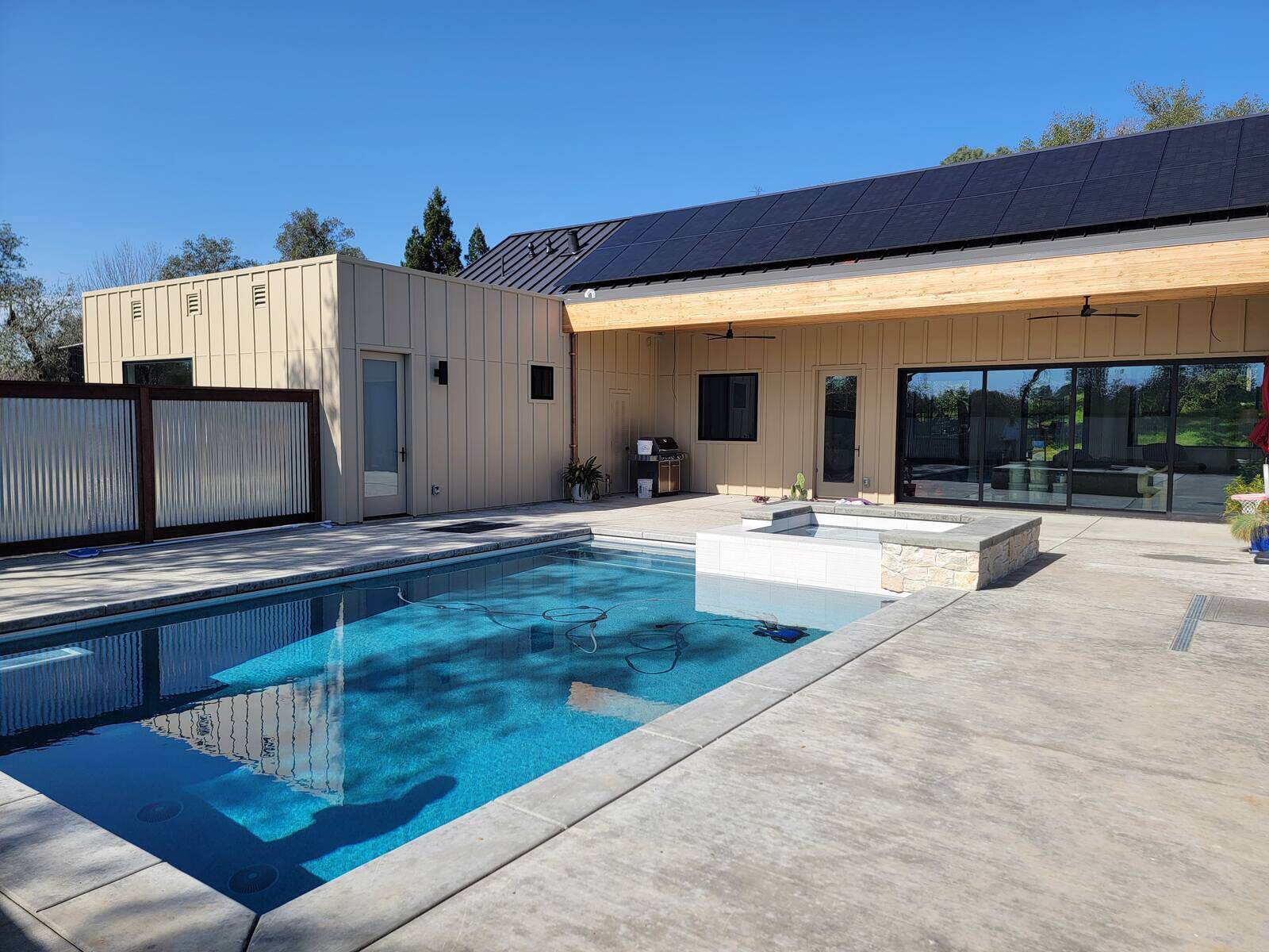 Backyard renovation featuring a sparkling swimming pool, spa, and sleek modern patio with solar-paneled roofing by H&H Builds in Sacramento, CA