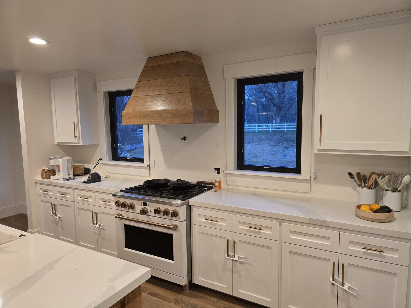 Modern kitchen remodel with white cabinets, wooden range hood, and black-framed windows by H&H Builds in Sacramento, CA