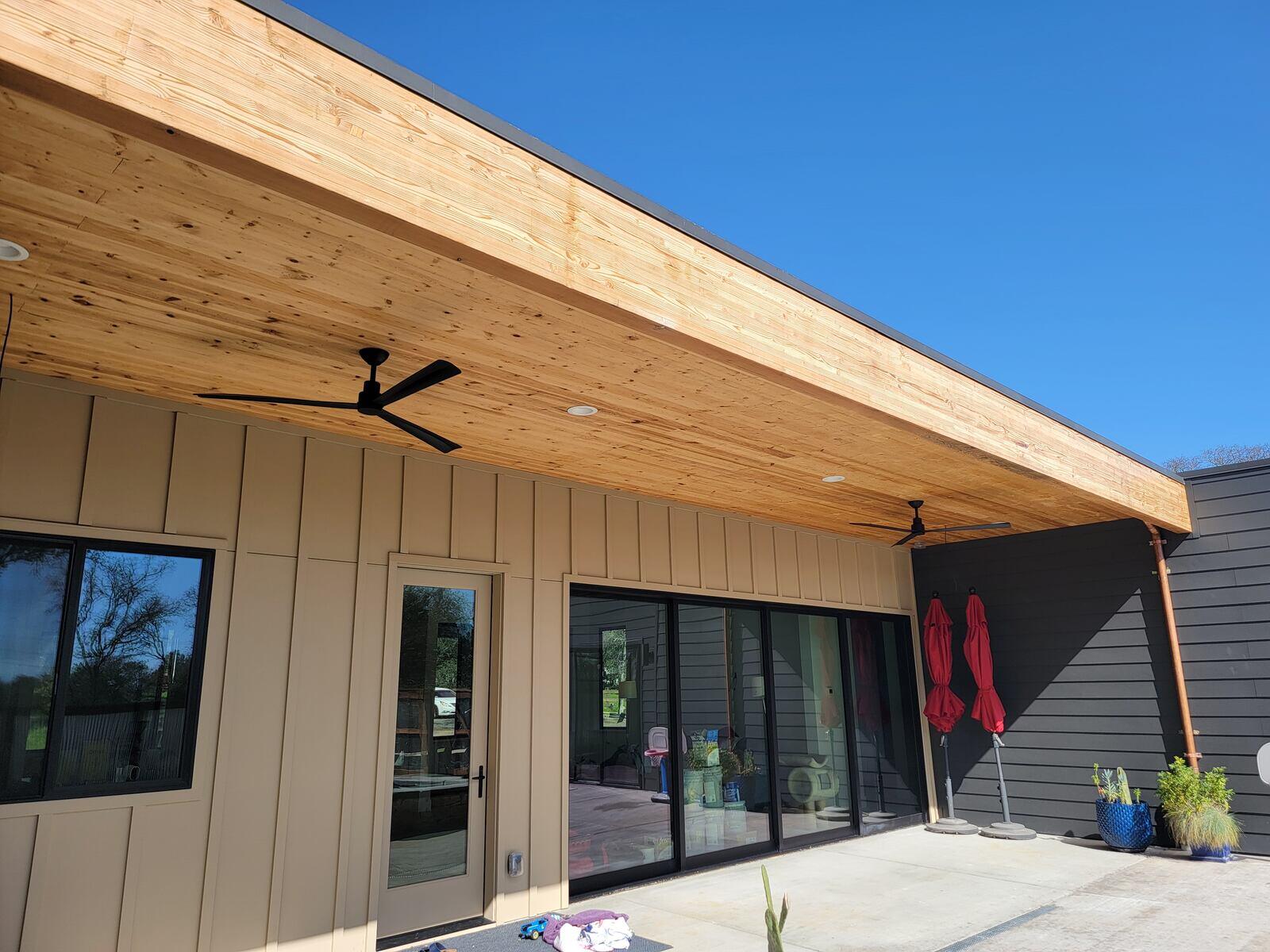 Outdoor patio renovation with a wooden ceiling, black fans, and modern glass doors completed by H&H Builds in Sacramento, CA