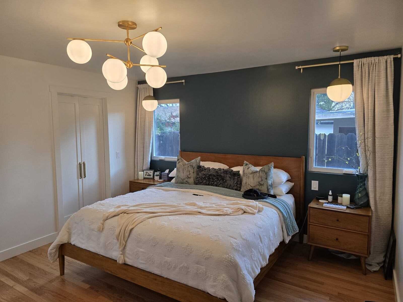 Remodeled master bedroom with green accent wall, modern gold chandelier, and wooden furniture by H&H Builds, Sacramento, CA